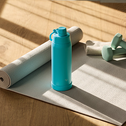 Blue water bottle on a yoga mat with a towel and weights in the background
