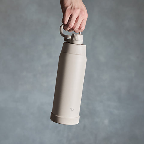 Beige thermos bottle held by a hand against a gray background