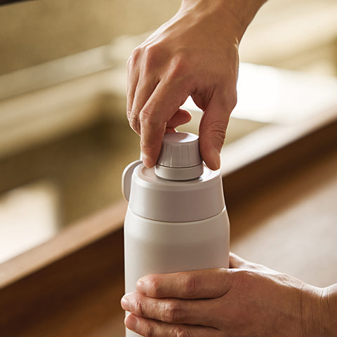 Person opening a white thermos with a blurred background