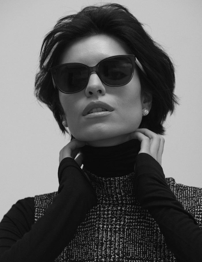 Anne Klein black acetate cat-eye sunglasses with dark smoke lenses and braided temple detail, worn front-facing.