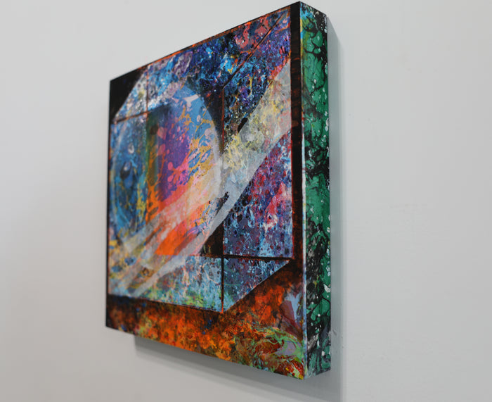 The artwork 'Galaxy Delivery' by Millie Benson features vibrant abstract geometric shapes with cosmic-inspired textures. Bold blues, oranges, and emerald greens swirl across layered angular forms, creating depth through mixed media techniques. The composition combines spray paint's ethereal effects with gouache's rich opacity on wood, suggesting an interstellar portal or cosmic landscape.