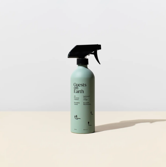 Spray bottle labeled 'Guests on Earth' on a light beige background